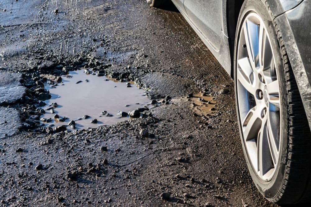 Car wheel close-up near a pothole on the broken road.
